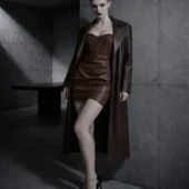 Robe bustier en cuir Aspa marron portée avec long manteau cuir ton sur ton, mannequin rousse appuyée contre mur béton