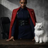 Harnais cuir Valdis noir, mannequin penchée sur table en bois, chat blanc à collier, manteau rouge militaire
