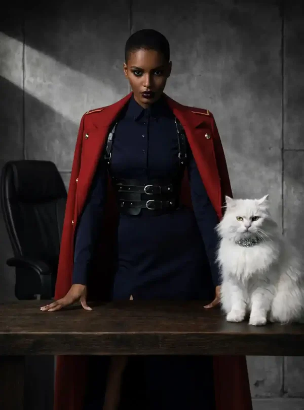 Harnais cuir Valdis noir, mannequin penchée sur table en bois, chat blanc à collier, manteau rouge militaire